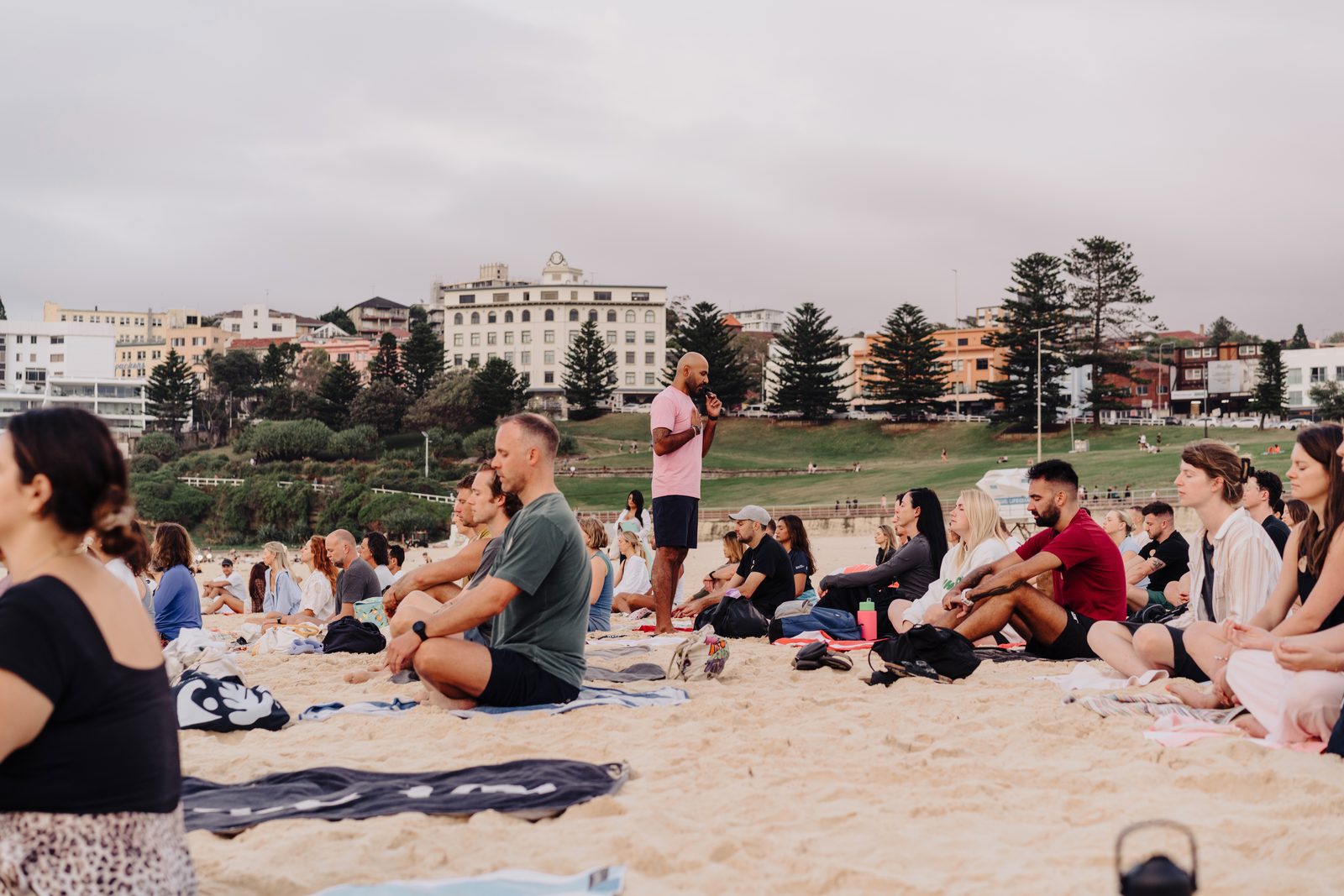 A group meditation and breathwork workshop led by Navjot Matharu on Bondi Beach, with participants seated on the sand